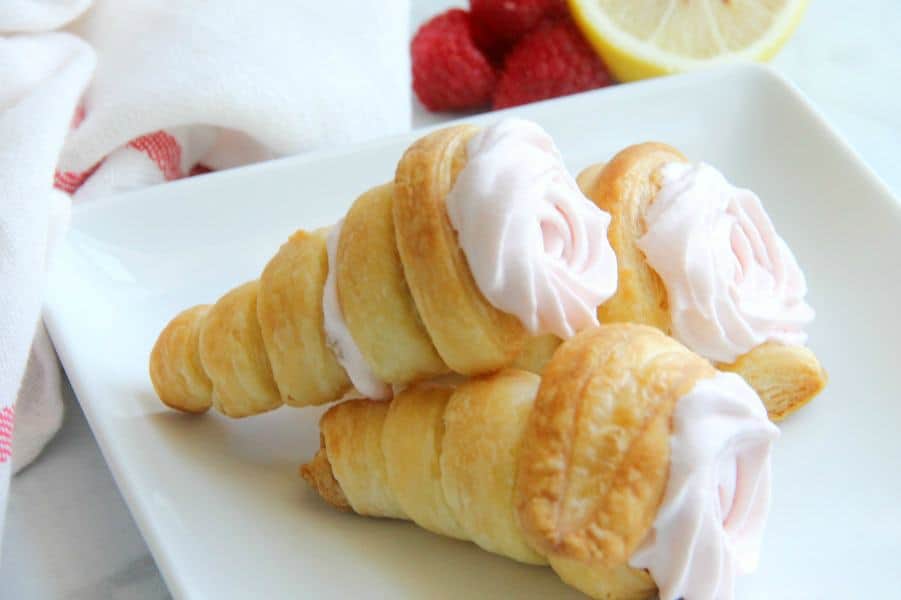 Lemon Raspberry Cream Horns! Made with buttery puff pastry and a homemade lemon raspberry whipped cream! The best dessert around! Lemon Raspberry Cream Horns stacked on white plate with raspberries and lemon