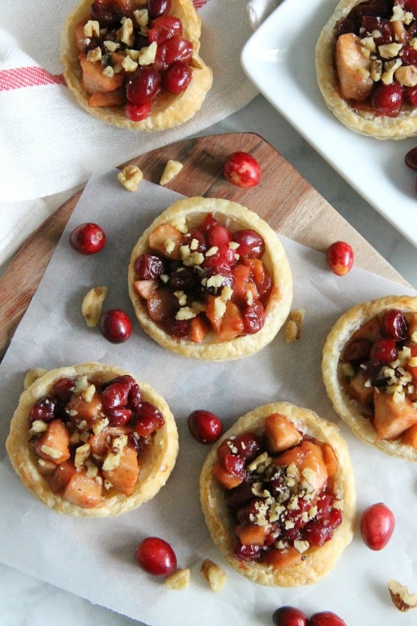 These Cranberry Apple Walnut Tarts would be the perfect addition to your holiday dessert table! Perfect for when you want to make individual desserts! | The Bitter Side of Sweet #cranberry #walnut #puffpastry #apple Cranberry Apple Walnut Tarts on brown board