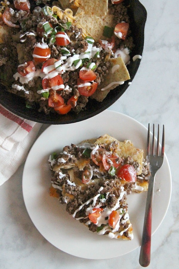 Taco Skillet Nachos are the best kind of party food! All of your favorite flavors for tacos topped onto a bed of tortilla chips for a delicious appetizer! | The Bitter Side of Sweet #gameday #appetizer #taco Taco Skillet Nachos on white plate