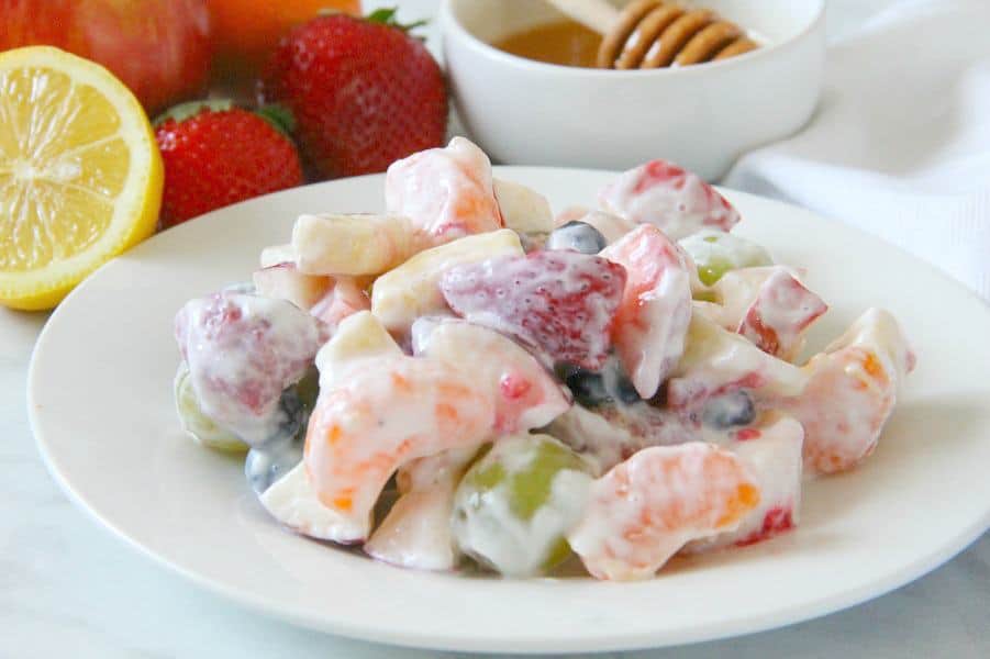 Creamy Yogurt Fruit Salad is a delicious alternative to a sweet dessert! Packed with lots of fruit, greek yogurt and honey, this salad will not disappoint! Creamy Yogurt Fruit Salad on white plate