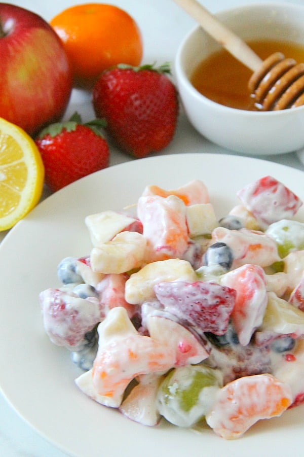 Creamy Yogurt Fruit Salad is a delicious alternative to a sweet dessert! Packed with lots of fruit, greek yogurt and honey, this salad will not disappoint! Creamy Yogurt Fruit Salad on white plate