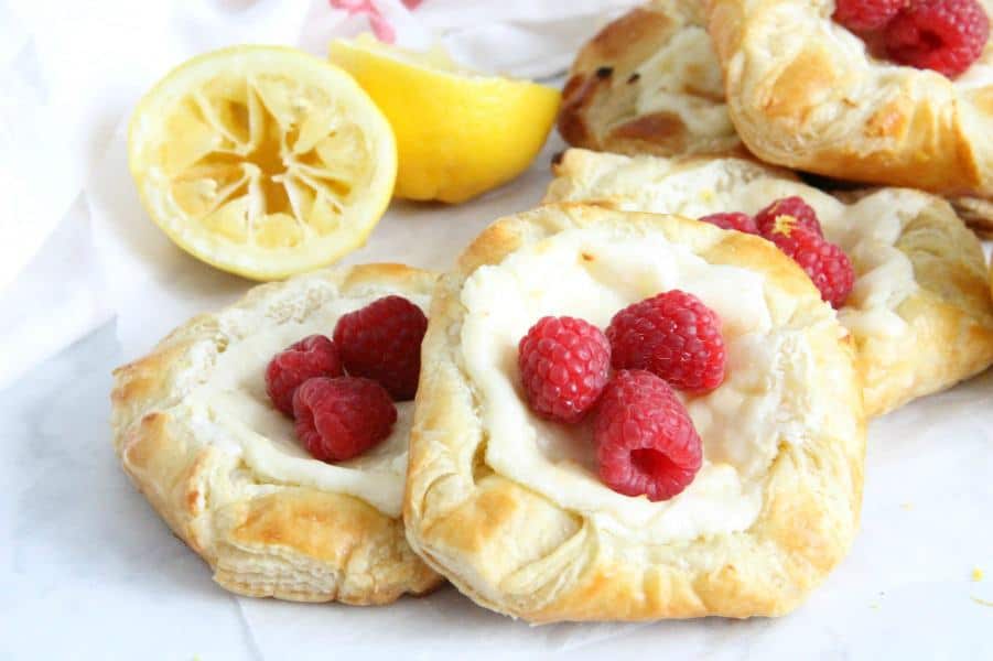 Start your day with a Lemon Raspberry Danish! You'll be so glad you did. With a warm cheese filled center and butter pastry this is perfection! Lemon Raspberry Danish on parchment paper