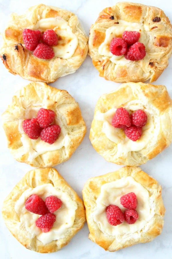 Start your day with a Lemon Raspberry Danish! You'll be so glad you did. With a warm cheese filled center and butter pastry this is perfection! Lemon Raspberry Danish on parchment paper
