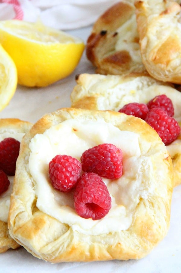 Start your day with a Lemon Raspberry Danish! You'll be so glad you did. With a warm cheese filled center and butter pastry this is perfection! Lemon Raspberry Danish on parchment paper