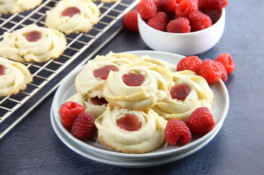 Raspberry Butter Cookies are sweet, simple, and perfect for gifting. Light, crisp butter cookies with a dollop of raspberry jam are great with a cup of tea! Raspberry Butter Cookies on white plate