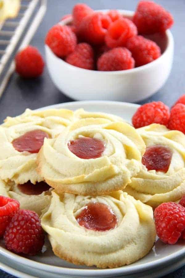 Raspberry Butter Cookies are sweet, simple, and perfect for gifting. Light, crisp butter cookies with a dollop of raspberry jam are great with a cup of tea! Raspberry Butter Cookies with fresh raspberries