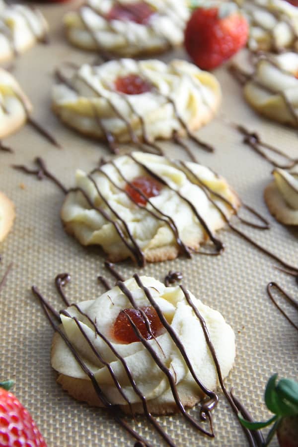 These Strawberry Chocolate Butter Cookies are a fun twist to the classic Italian Butter Cookie! So delicious with strawberry jam and chocolate drizzle! Strawberry Chocolate Butter Cookies on brown background