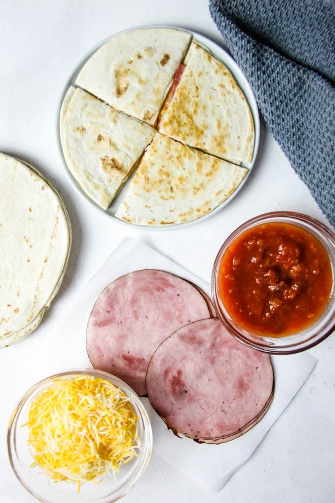 Easy Ham and Cheese Quesadillas made with 3 ingredients and perfect for a quick lunch or snack! Flour tortillas topped with deli ham and Mexican cheese! Ham and Cheese Quesadillas ingredients on white back ground