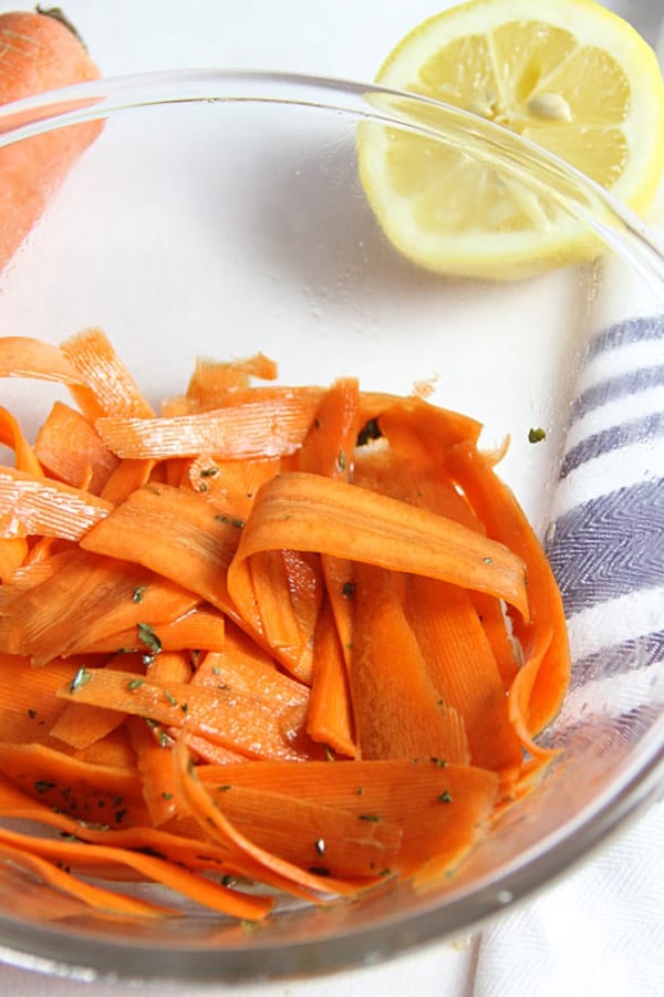 This fresh Lemon Carrot Salad is made with just 5 ingredients! With a simple dressing topped over shaved carrots this makes a simple side dish. Lemon Carrot Salad in glass bowl with half lemon