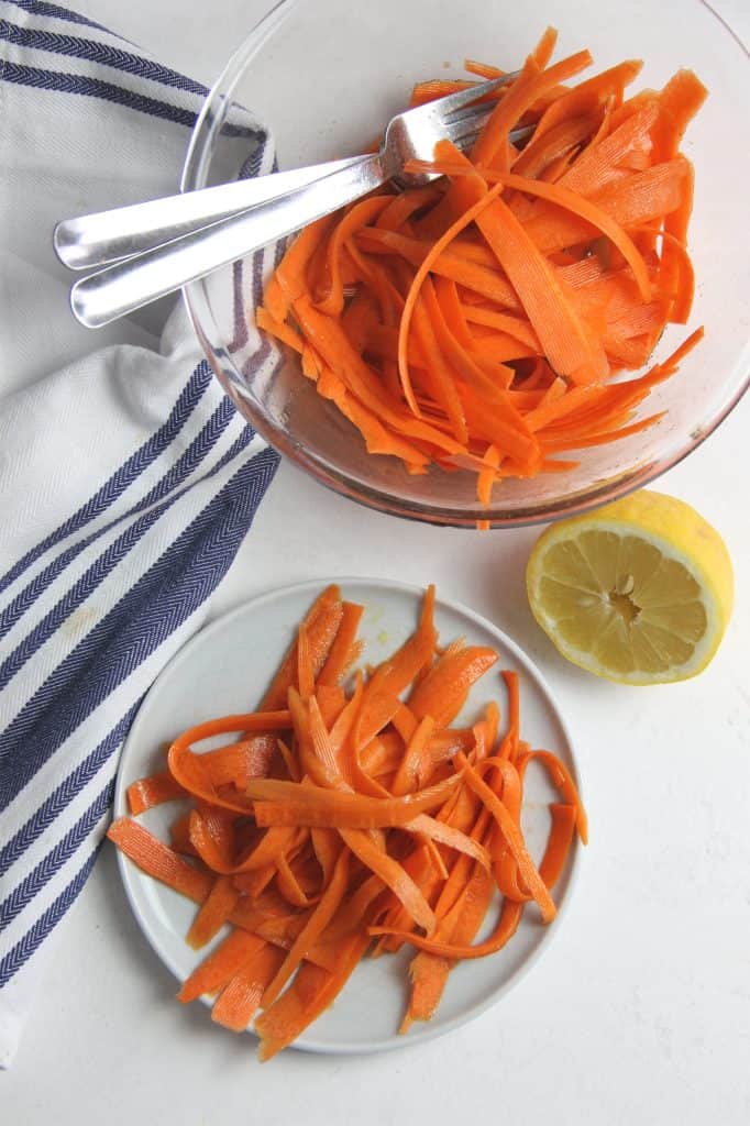 This fresh Lemon Carrot Salad is made with just 5 ingredients! With a simple dressing topped over shaved carrots this makes a simple side dish. Lemon Carrot Salad in glass bowl with forks and on plate