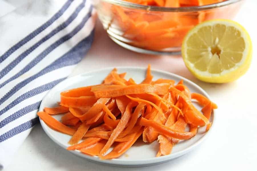 This fresh Lemon Carrot Salad is made with just 5 ingredients! With a simple dressing topped over shaved carrots this makes a simple side dish. Lemon Carrot Salad on white plate with lemon