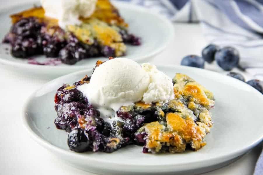 Easy Homemade Blueberry Cobbler! With an easy buttery crust mixed with fresh or frozen blueberries, this is the perfect fruit dessert! Blueberry Cobbler on white plate with ice cream