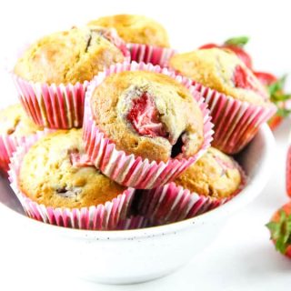 Strawberry Oatmeal Muffins in pink liners stacked in white bowl with fresh strawberries