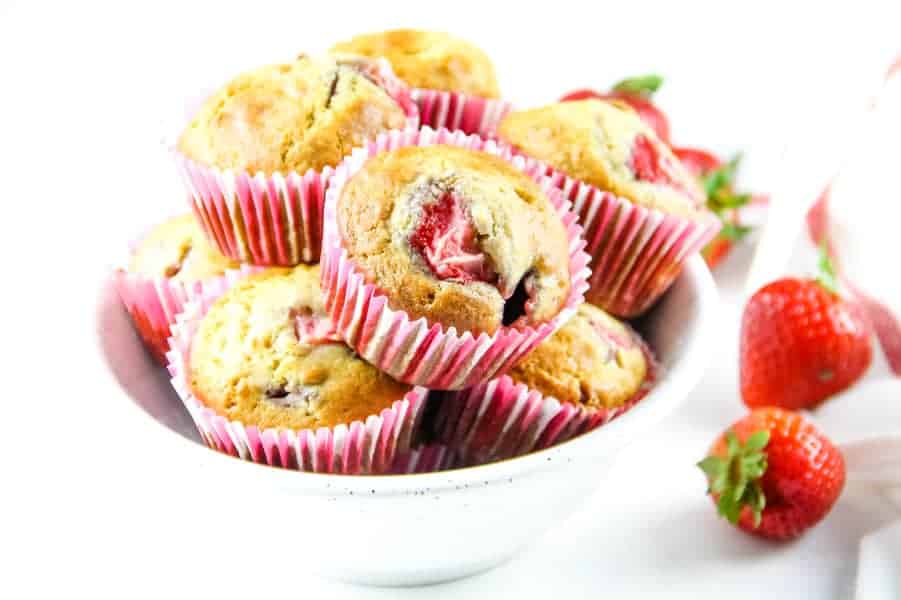 Strawberry Oatmeal Muffins are a hearty, soft breakfast muffin! Studded with fresh strawberries, these portable muffins will become a delicious favorite! Strawberry Oatmeal Muffins in pink liners stacked in white bowl with fresh strawberries