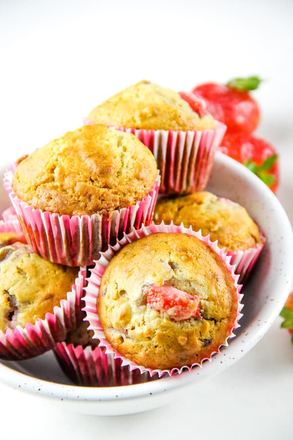 Strawberry Oatmeal Muffins are a hearty, soft breakfast muffin! Studded with fresh strawberries, these portable muffins will become a delicious favorite! Strawberry Oatmeal Muffins stacked in white bowl with fresh strawberries