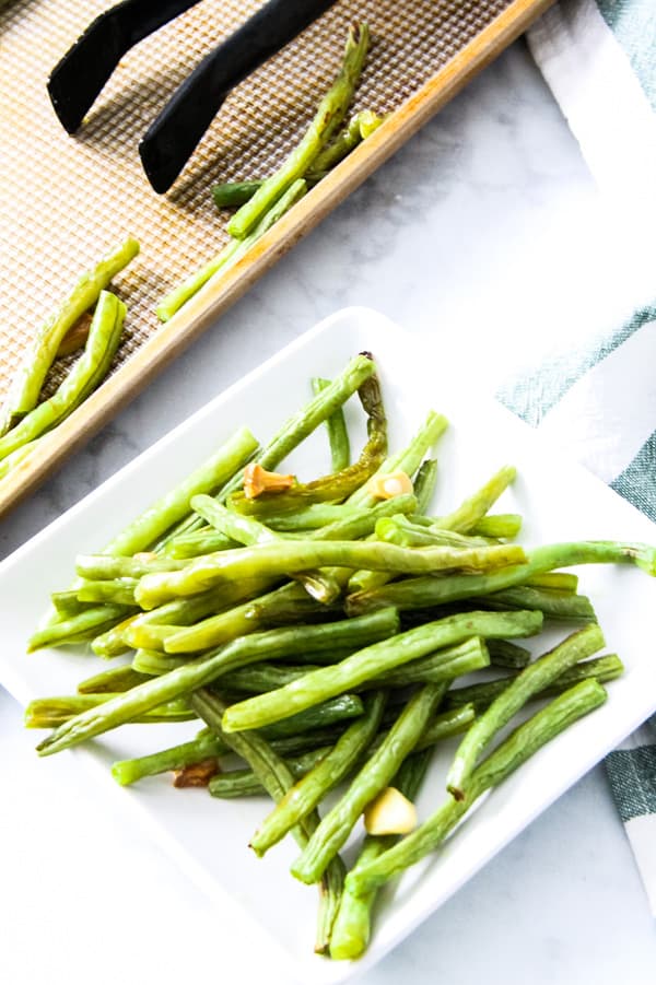 These easy sheet pan Roasted Green Beans are the simplest side dish ever! With just 4 ingredients and 20 minutes they will be cooked to perfection! Sheet Pan Roasted Green Beans overhead view of green beans on white plate