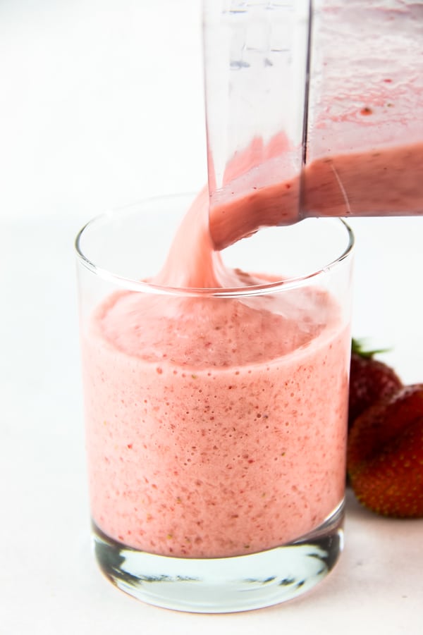 Strawberry Banana Smoothie is so creamy and delicious! Full of strawberry flavor with a touch of banana! Makes for a perfect post workout treat! Strawberry Banana Smoothie being poured into glass
