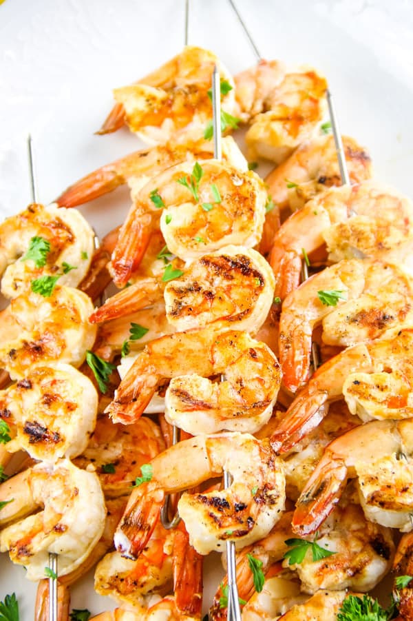 Easy Grilled Lemon Shrimp Skewers made with just 5 ingredients! Can be cooked on a grill or even in the oven! Grilled Lemon Shrimp Skewers on metal skewers stacked on white plate