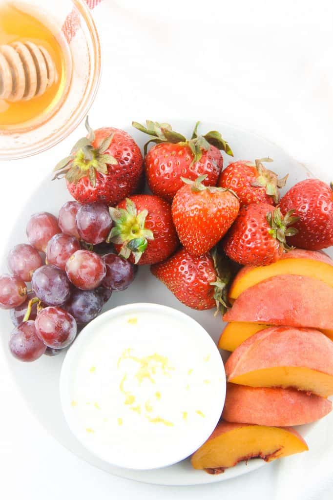 This Easy Honey Yogurt Dip is flavored with honey, lemon zest and vanilla! Top this homemade with granola or serve with fresh fruits! Honey Yogurt Dip overhead view in white bowl topped with lemon zest