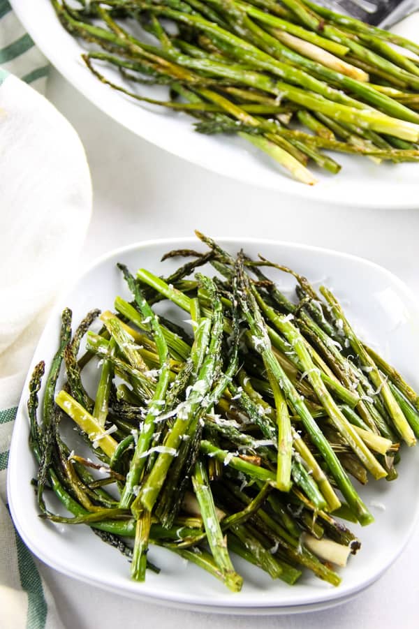 Easy Sheet Pan Roasted Asparagus coated in olive oil, fresh garlic and salt! This simple side dish is the easiest way to make asparagus! Sheet Pan Roasted Asparagus on small white plate cut into small pieces