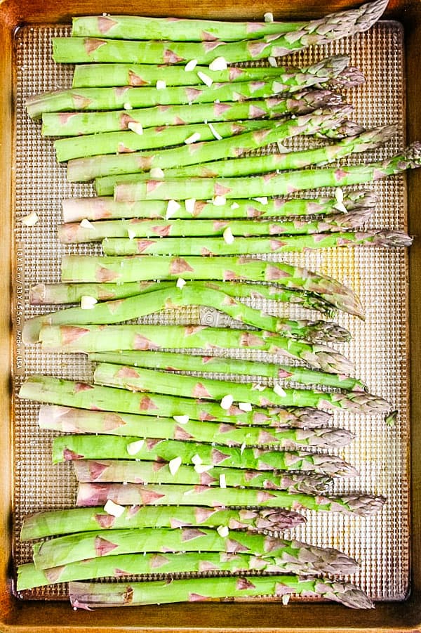 Easy Sheet Pan Roasted Asparagus coated in olive oil, fresh garlic and salt! This simple side dish is the easiest way to make asparagus! Sheet Pan Roasted Asparagus uncooked on sheet pan