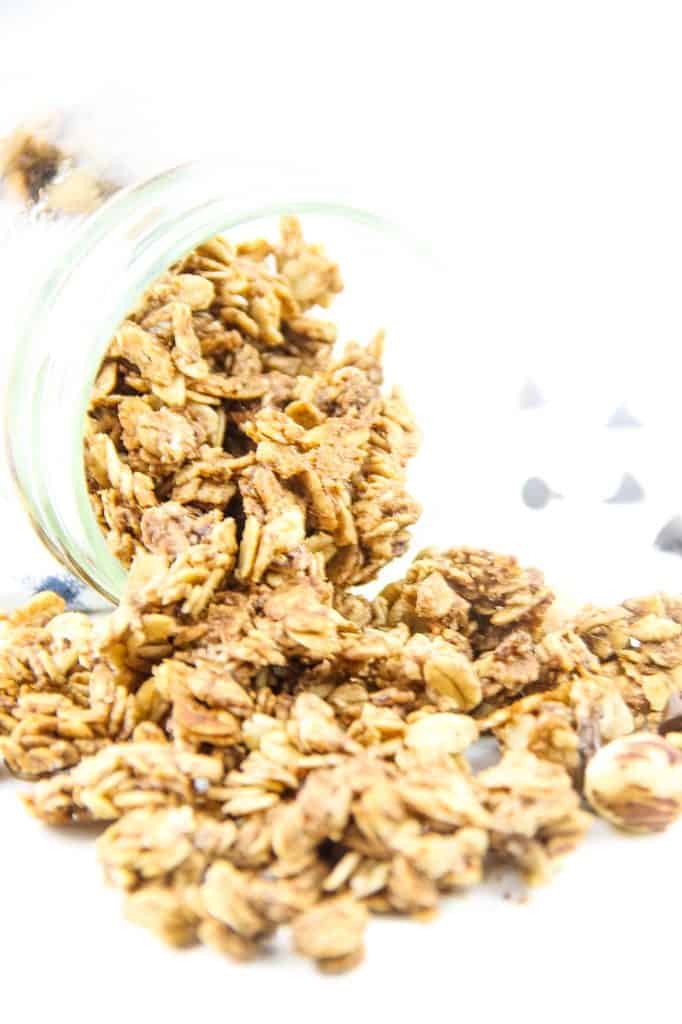 This Chocolate Hazelnut Granola is perfect for snacking! Made with nutella, oats, maple syrup and canola oil! Simple and easy! Chocolate Hazelnut Granola spilling out of glass jar