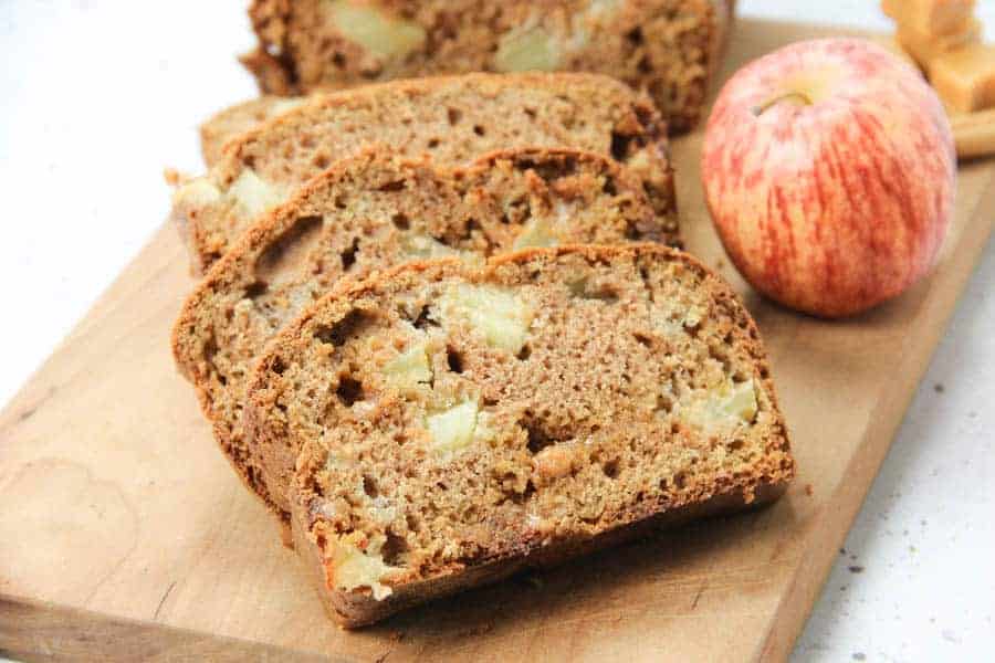 using all whole wheat flour, dried cranberries and pumpkin seeds. Caramel Apple Bread on brown cutting board in slices