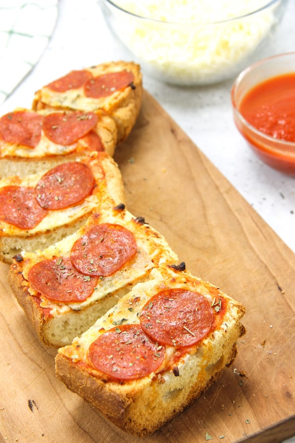 Super simple Pepperoni French Bread Pizza! Bakes up in 15 minutes! Cheesy, full of spices with a crunchy french bread crust! Pepperoni French Bread Pizza sliced on cutting board