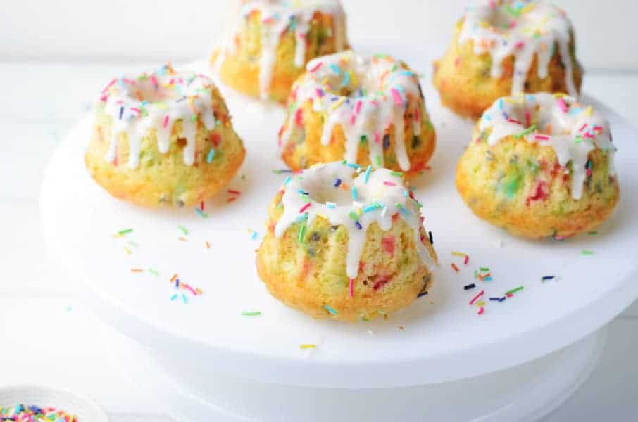 These homemade Funfetti Mini Bundt Cakes are perfect for any celebration! Made with simple ingredients and lots of sprinkles! Funfetti Mini Bundt Cakes with 6 cakes on white cake plate