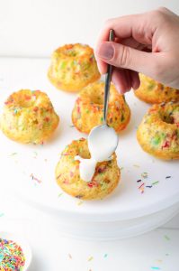 Funfetti Mini Bundt Cakes with spoon drizzling glaze