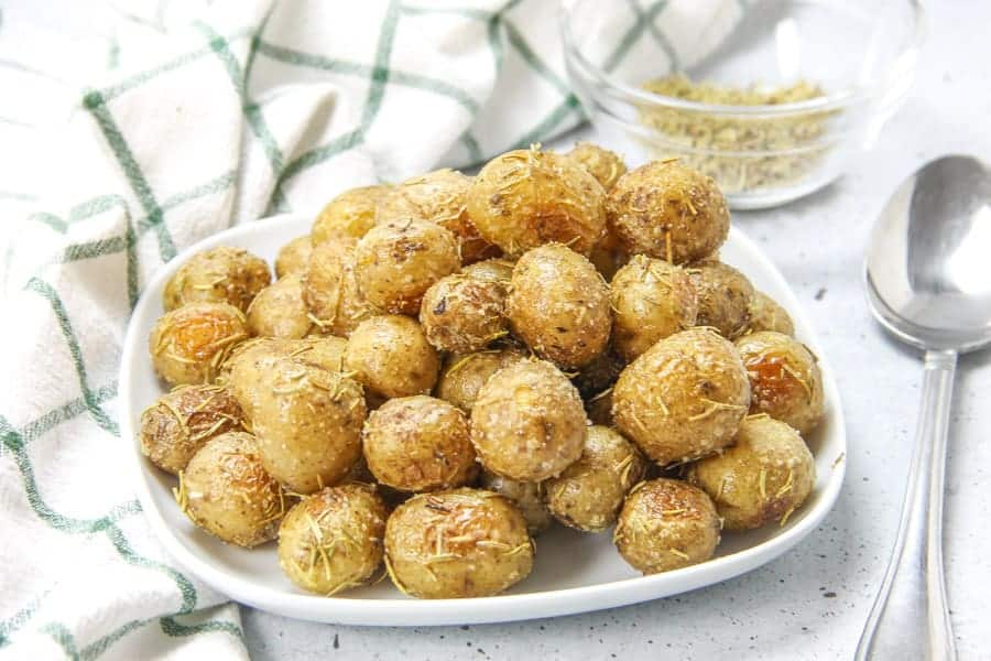 Roasted Rosemary Potatoes bakes up quick and easy! Creamy potatoes loaded with rosemary, for the best side dish! Roasted Rosemary Potatoes on white plate with spoon