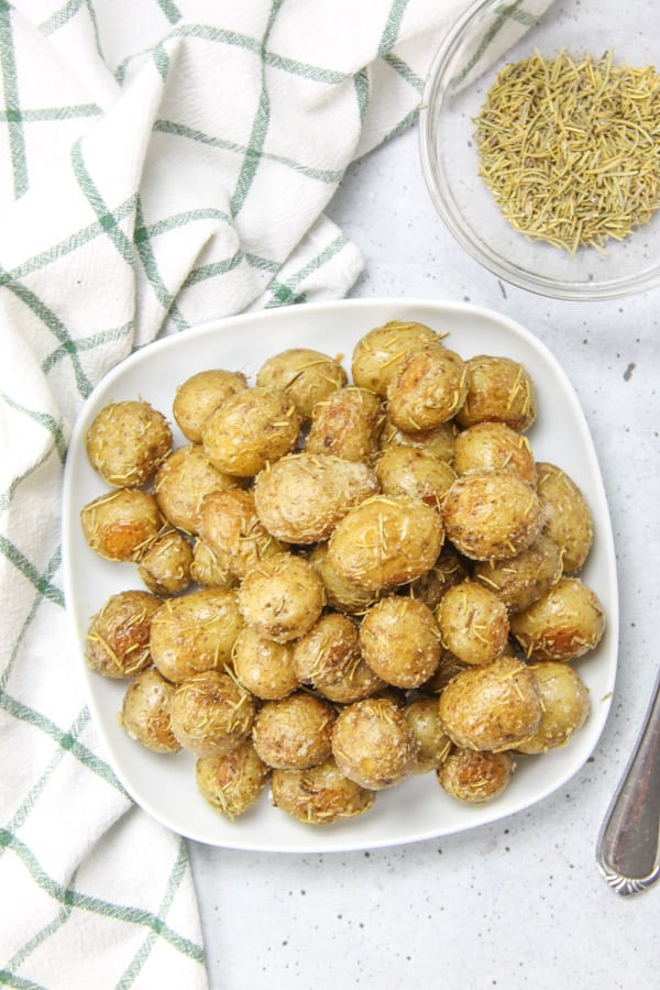 Roasted Rosemary Potatoes bakes up quick and easy! Creamy potatoes loaded with rosemary, for the best side dish! Roasted Rosemary Potatoes overhead shot on white plate
