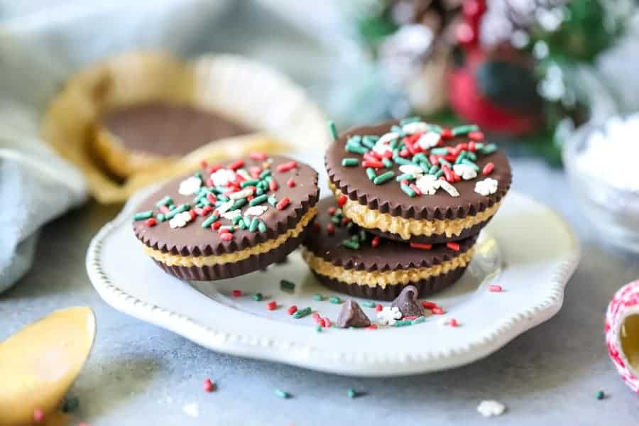 Easy Homemade Peanut Butter Cups! Layers of rich chocolate and creamy peanut butter, these are a fantastic treat! Perfect for freezing too! Homemade Peanut Butter Cups stacked on white plate with holiday sprinkles