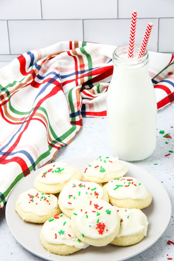 These classic Soft Sugar Cookies are perfect for a baking day! With a buttercream frosting and fun sprinkles they will be a hit! Soft Sugar Cookies on white plate with milk in a jug