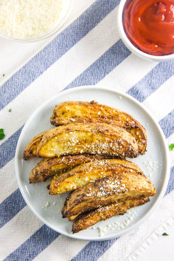 These easy to make Air Fryer Parmesan Potato Wedges cook up in just 20 minutes! Topped with flavors of basil, garlic and cheese! Air Fryer Parmesan Potato Wedges on plate with ketchup.