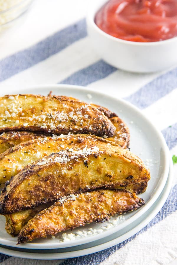 These easy to make Air Fryer Parmesan Potato Wedges cook up in just 20 minutes! Topped with flavors of basil, garlic and cheese! Air Fryer Parmesan Potato Wedges on white plate with extra cheese.