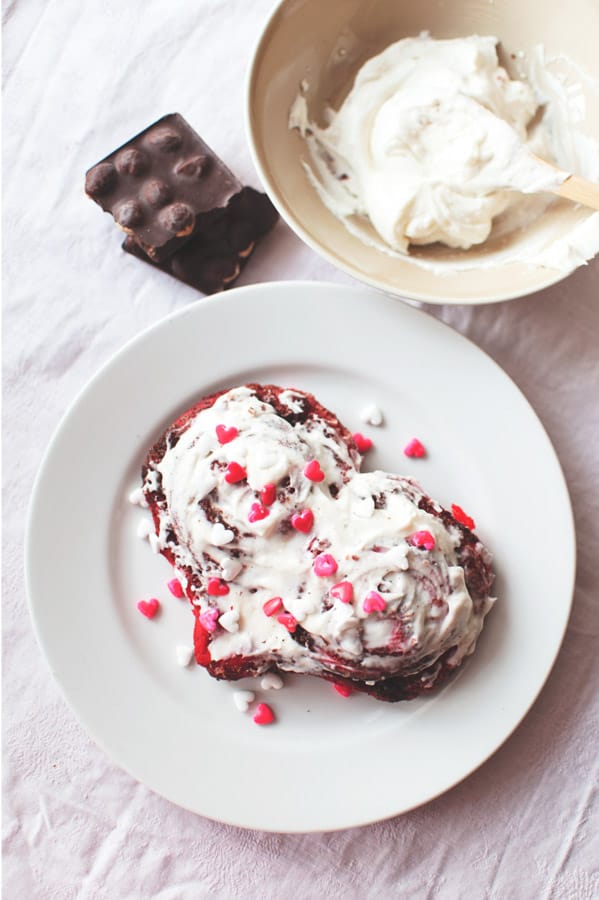 These Red Velvet Cinnamon Rolls are such a fun treat for breakfast or brunch! Made with a homemade dough and topped with a gooey frosting! Red Velvet Cinnamon Rolls on plate with sprinkles
