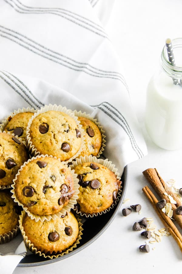 These Chocolate Chip Oatmeal Cookies are delicious for a grab and go breakfast! Made with oats, chocolate chips and a touch of cinnamon! muffins stacked in gray bowl with glass of milk.
