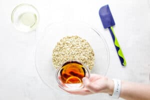 pour in maple syrup in glass bowl with oats.