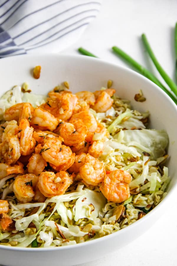 Delicious, but simple Shrimp Ramen Salad! With spicy shrimp, toasted almonds, sunflower seeds and a shrimp flavored dressing! Shrimp Ramen Salad in white bowl.