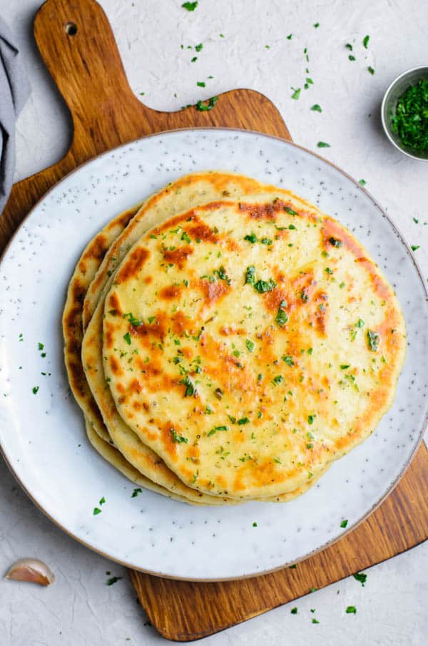 Easy Homemade Flatbread will be the only flatbread you will ever need! Learn how to make these soft, spongy, filled with herbs bread! flatbread stacked on plate on wooden cutting board.