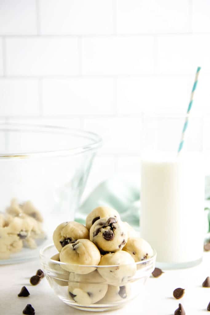These easy no bake Cookie Dough Bites are made with a few simple ingredients! They are rolled into balls, eaten with a spoon or can be frozen! Cookie Dough Bites stacked in glass bowl.