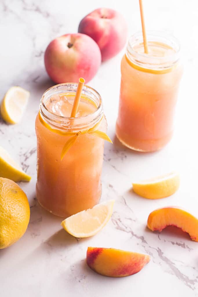 This simple, refreshing Peach Black Tea Lemonade has the perfect blend of flavors and just a touch of sweetness! Perfect for hot summer days! Peach Black Tea Lemonade on white background with peaches sliced up.