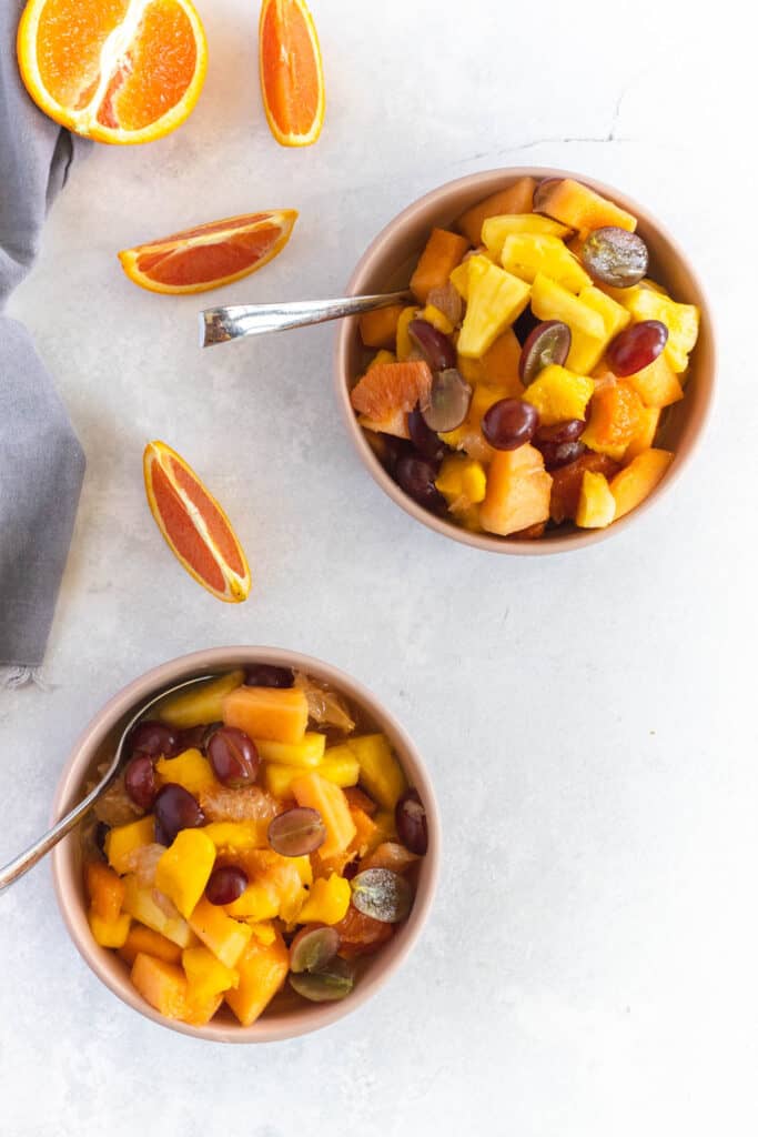 This Citrus Fruit Salad is so simple to put together! With seasonal fruit and a splash of orange juice this salad is long lasting! Citrus Fruit Salad in two bowls with orange slices on background.