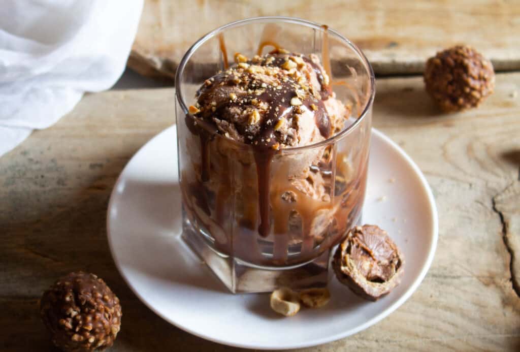 No churn Ferrero Rocher Ice Cream! A delicious creamy hazelnut chocolate ice cream that is the ultimate summer treat! Ferrero Rocher Ice Cream in glass cup on white plate.