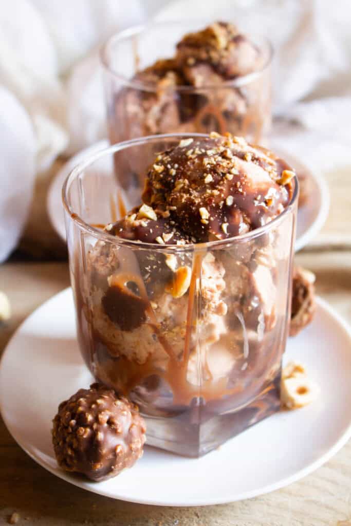 No churn Ferrero Rocher Ice Cream! A delicious creamy hazelnut chocolate ice cream that is the ultimate summer treat! Ferrero Rocher Ice Cream in glass cup topped with chocolate.