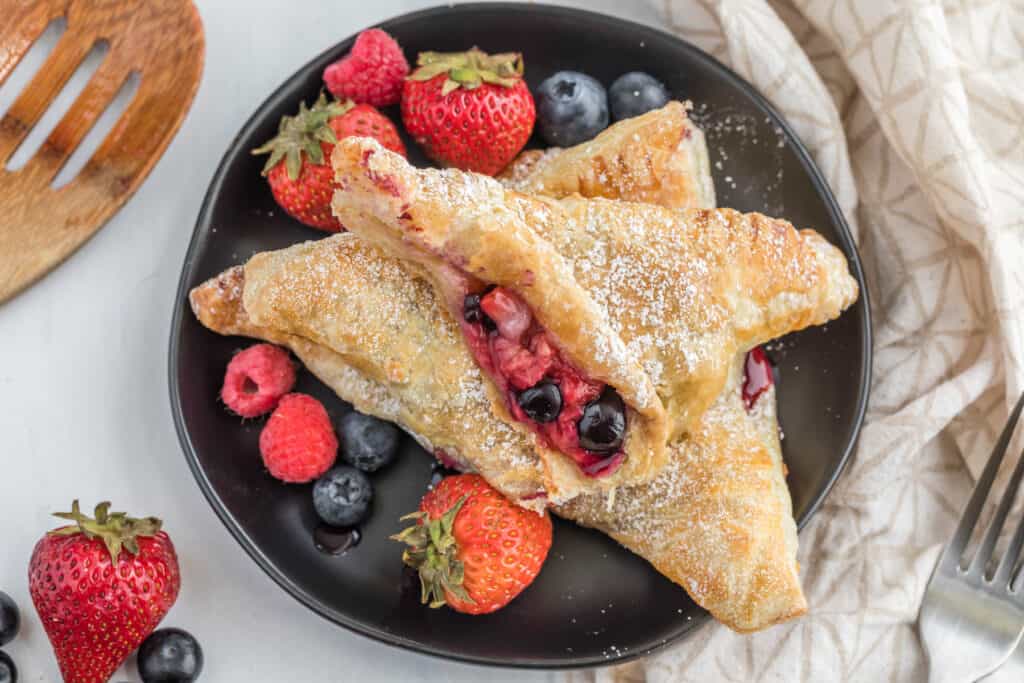 Mixed Berry Turnovers can brighten up your breakfast or your dessert. They are ready in less than half an hour, too! Use any kind of fresh berry you want! mixed berry turnover cut in half on plate.