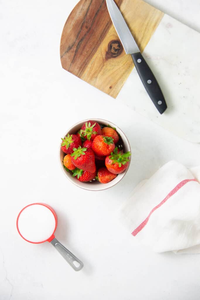This Easy Strawberry Sauce Recipe is made with just two ingredients and there is no cooking involved! Perfect on cake, ice cream, or granola! Easy Strawberry Sauce Recipe ingredients on white blackground.
