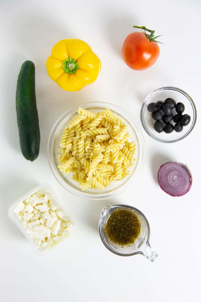 Easy Greek Pasta Salad served cold with a homemade vinaigrette. With fresh vegetables topped with feta cheese! Greek Pasta Salad ingredients in glass bowls.