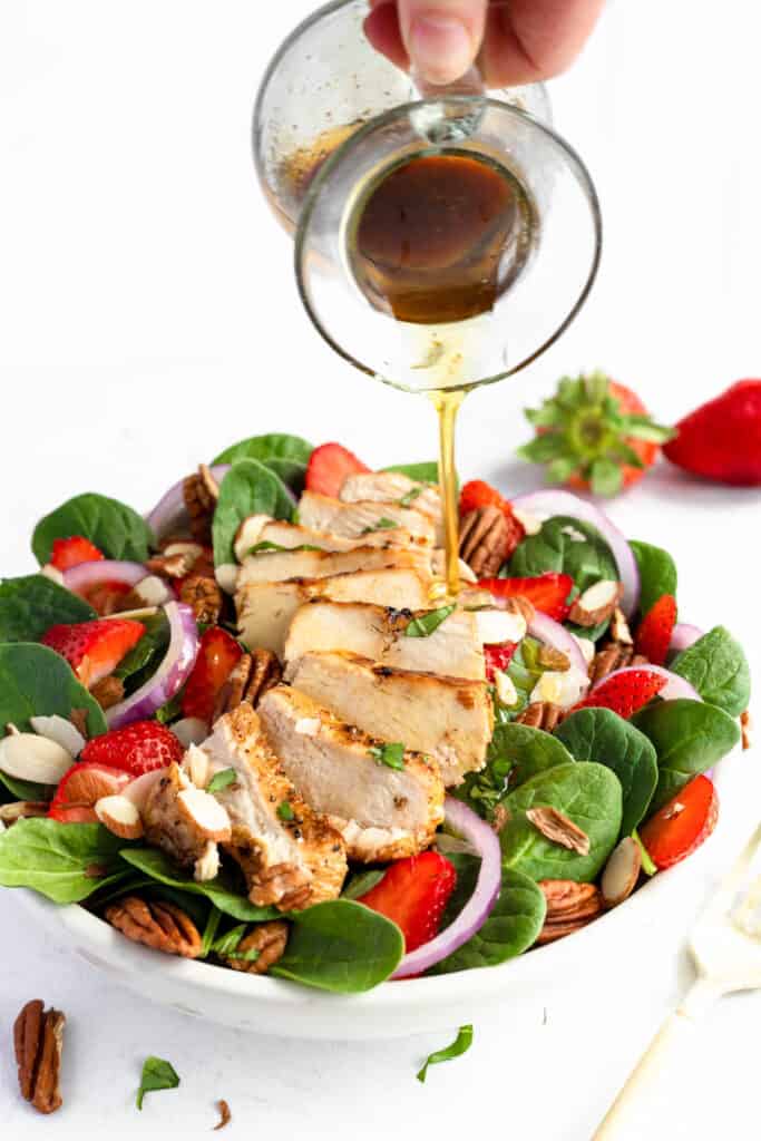 This easy Strawberry Chicken Spinach Salad is a delicious, complete meal! With marinated chicken, strawberries and a homemade vinaigrette! Drizzling dressing on Strawberry Chicken Spinach Salad.